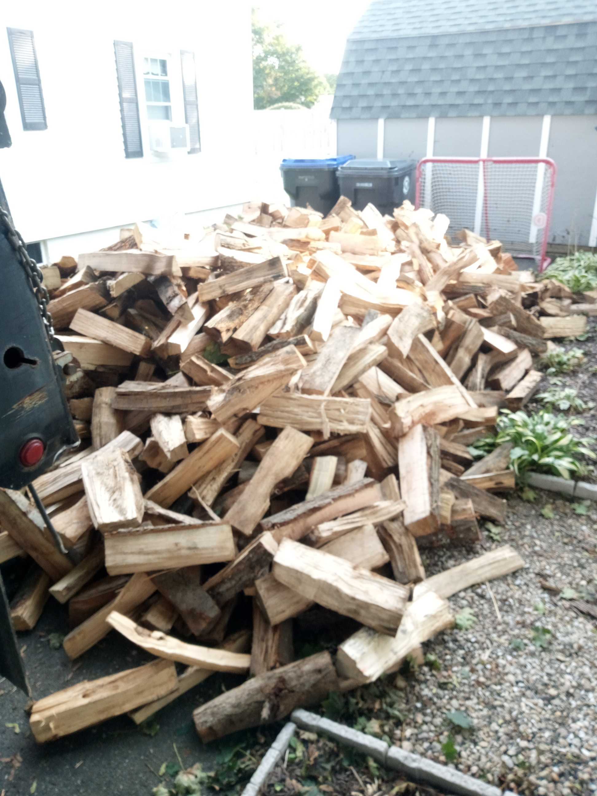 Freshly delivered firewood stacked beside a home and backyard fence